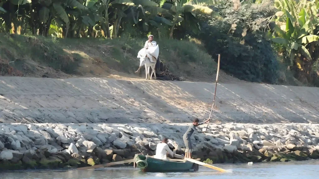 Local people navigating a small boat and walking along the Nile riverbank in Upper Egypt