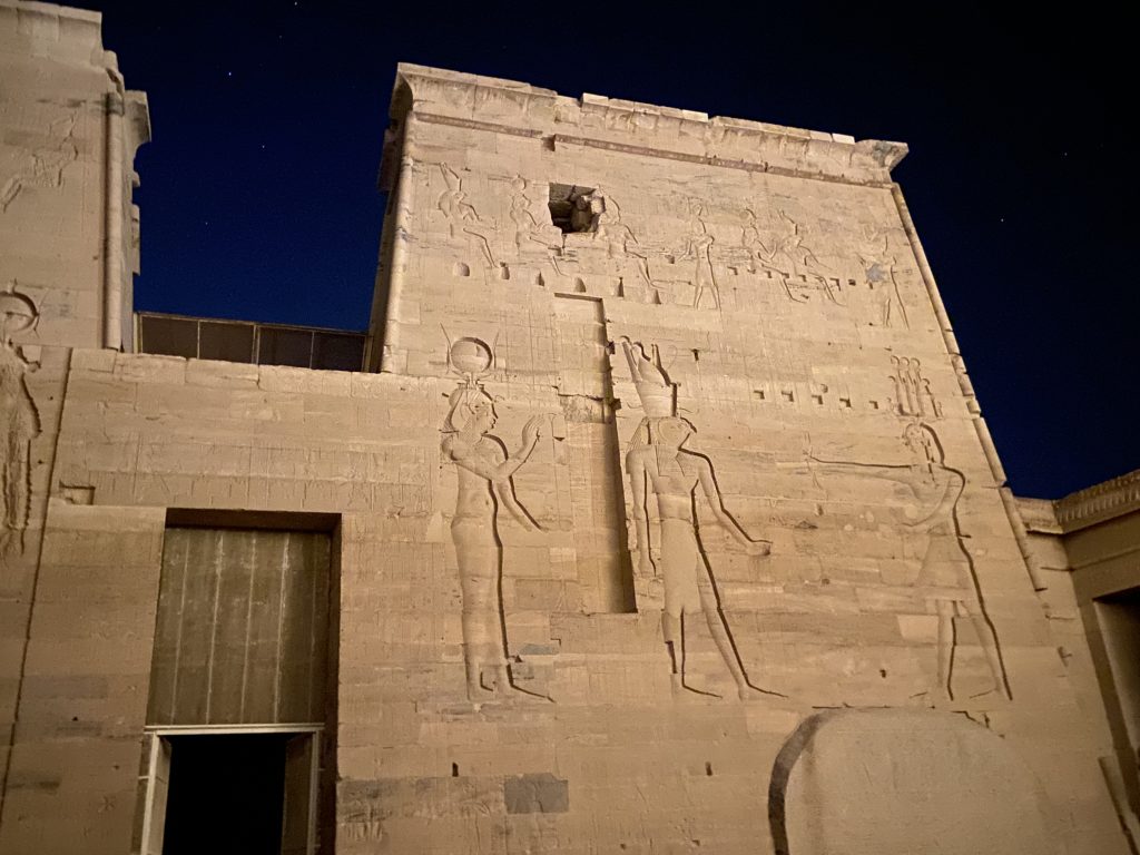 Ancient Egyptian carved reliefs of gods on the illuminated walls of Philae Temple at night in Aswan, Egypt