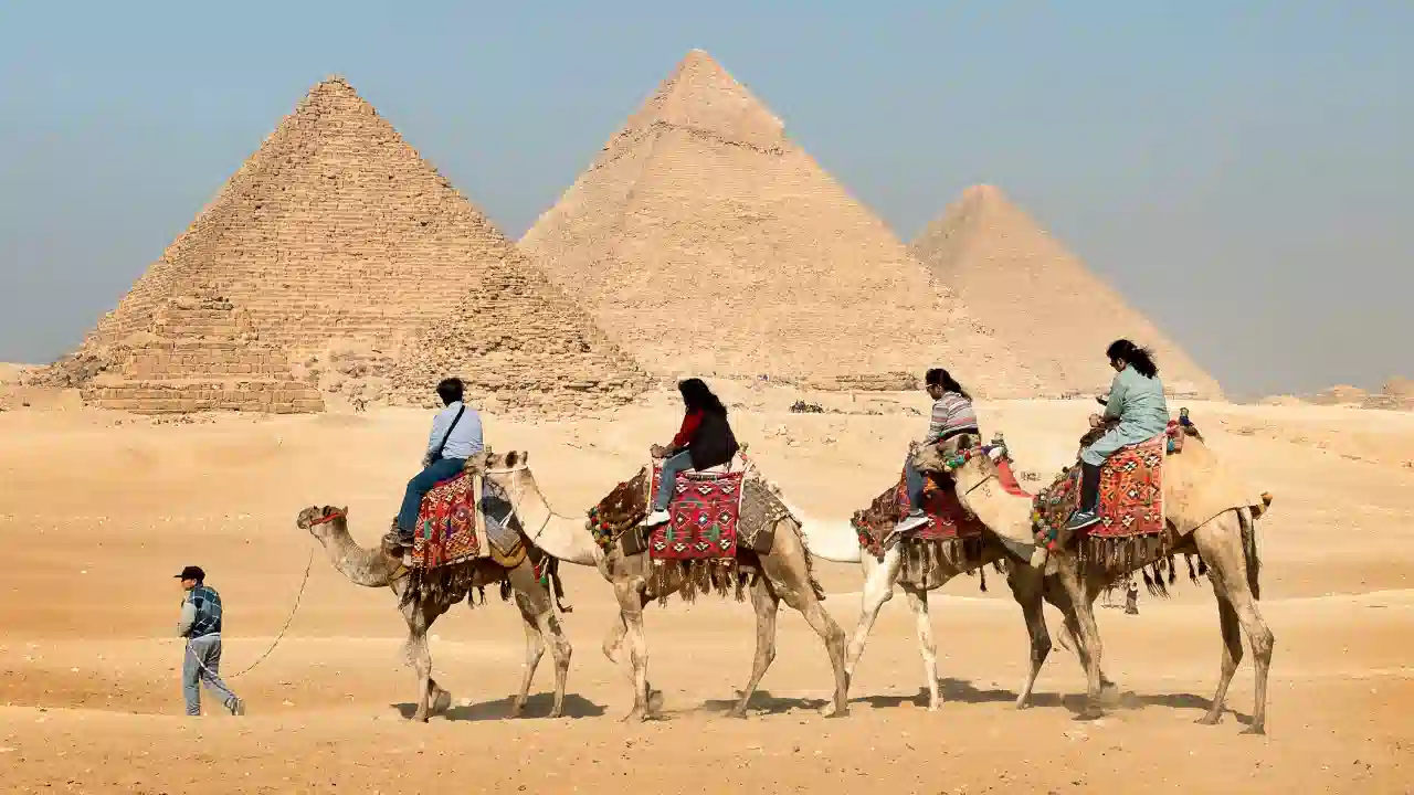 Tourists riding camels in front of the pyramids of Giza Egypt desert landscape