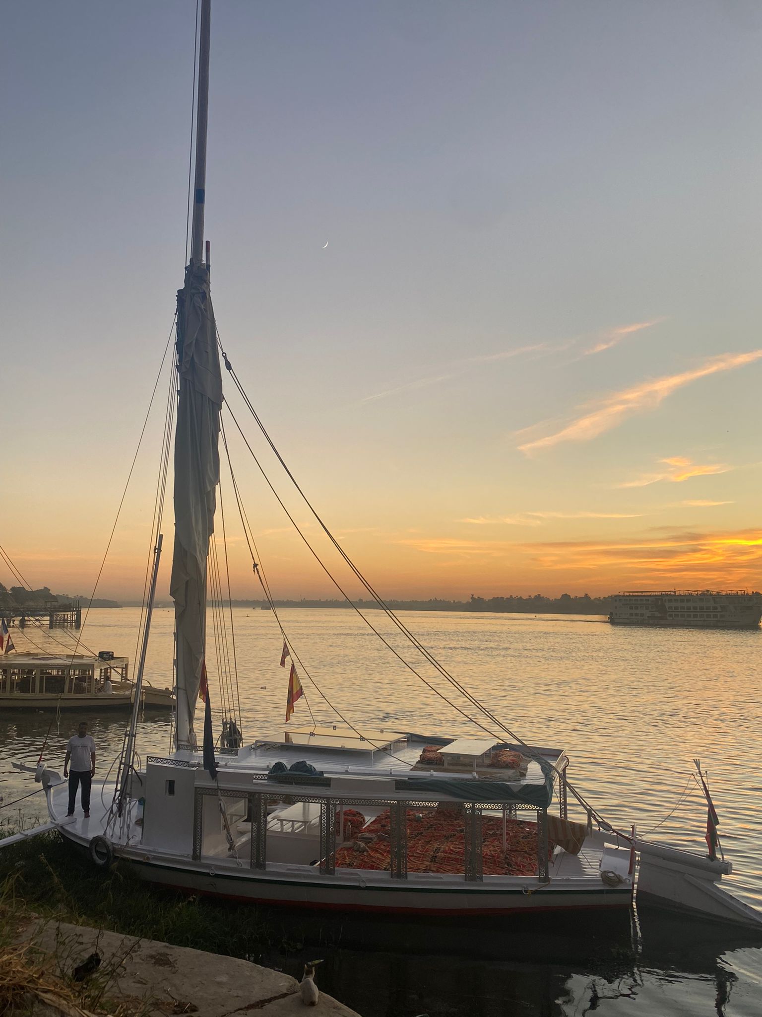 Felucca Maitea moored on the Nile River at sunset with golden sky and traditional sailing boat in Aswan, Egypt
