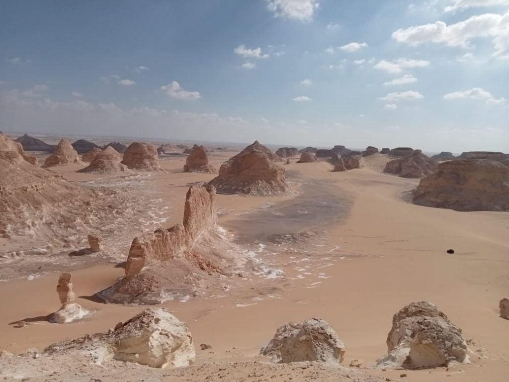 Panoramic landscape of chalk rock formations and sand dunes in Egypt’s White Desert under a blue sky
