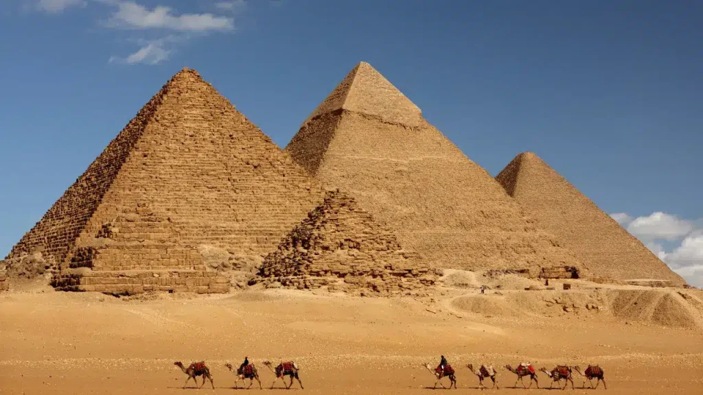 The pyramids of Giza with camels crossing the desert in Egypt under blue sky