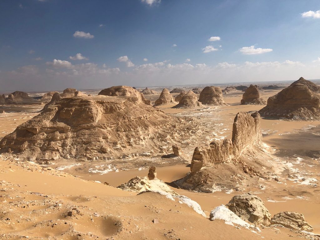 Layered sandstone rock formations and sand dunes in Egypt’s Western Desert under a blue sky