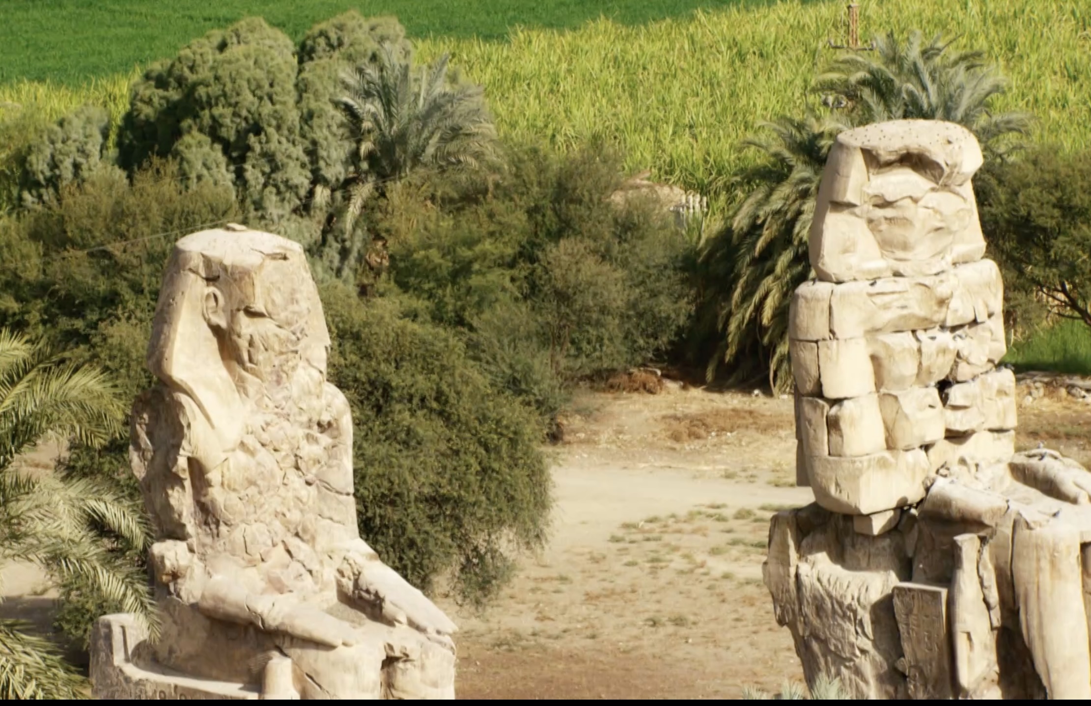 Colossi of Memnon ancient statues standing near green Nile fields in Luxor Egypt
