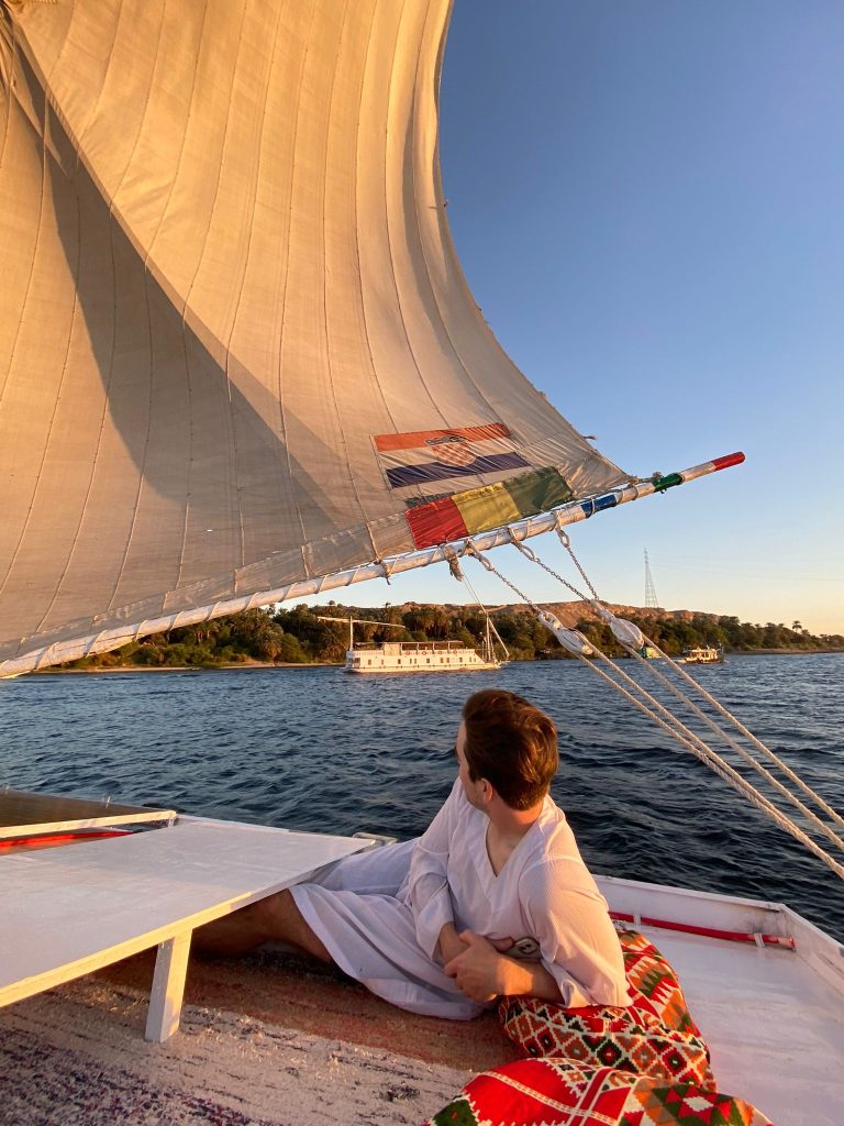 Traveler relaxing on a traditional felucca sailboat while sailing the Nile at sunset near Aswan Egypt